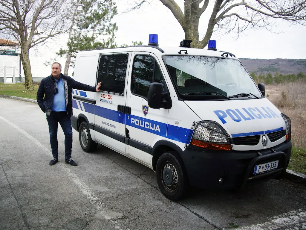 Martin, 61 Jahre, seit 43 Jahren Kriminalbeamter, vor einem Polizeiwagen mit der Aufschrift "Policija"